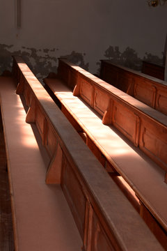 interior view of old church walls crumble and empty wooden pews without people, rows of wooden church benches lit by the sun through church windows