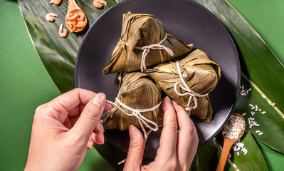 Zongzi, woman eating steamed rice dumplings on green table background, food in dragon boat festival duanwu concept, close up, copy space, top view, flat lay