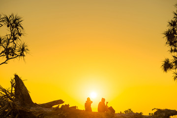 Silhouettes of romantic couple sitting on tree trunk at tropical beach at sunset