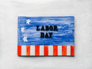 Obraz premium LABOR DAY. Notepad, American flag pattern and wooden letters of the alphabet on a white table. Close-up. Bright photo and space for your inscriptions. Congratulations to relatives, friends, colleagues