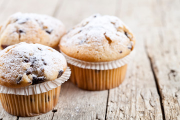 Homemade fresh muffins with sugar powder closeup on rustic wooden table background.