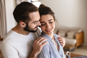Photo of gentle brunette couple in love smiling while hugging together in apartment