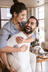 Photo of playful brunette couple in love smiling while hugging together in apartment