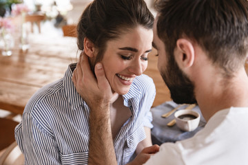 Photo of modest brunette couple in love smiling while hugging together in apartment