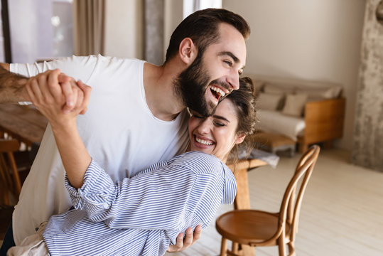 Photo of laughing brunette couple in love smiling while hugging together in apartment