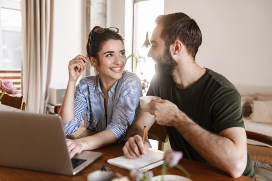 Image of successful brunette couple working on laptop together while sitting at table at home