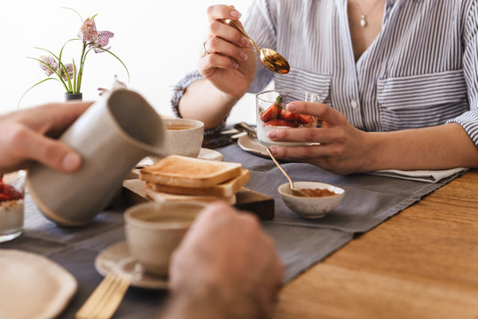 Image of lovely young couple eating together at table while having breakfast in apartment