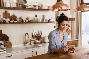 Photo of gorgeous brunette woman 20s eating panna cotta dessert with teaspoon at home
