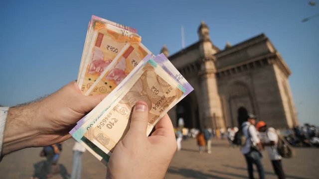 A man considers Indian rupees against the background of the Gate of India in the city of Mumbai. Hands close up.