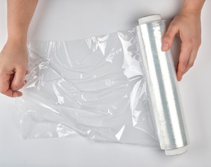 two hands hold a large roll of wound white transparent film for wrapping food