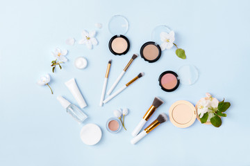 Face care and make up products with spring apple bloom (tonic or lotion, serum, cream, micellar water, cotton pads and makeup brushes) on blue background. Freshness and face care. Decorative cosmetics