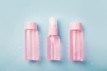 Three  bottles of pink tonic or lotion sprinkled with water on blue  background. Freshness and body care. Female cosmetics. Micellar water. Travel set of face care cosmetic