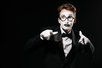 portrait of mime man in tuxedo and glasses points at you on black background