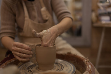 Fototapeta na wymiar Potter working on potters wheel making ceramic pot from clay in pottery workshop