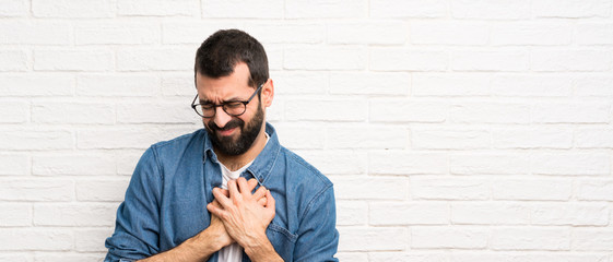 Handsome man with beard over white brick wall having a pain in the heart