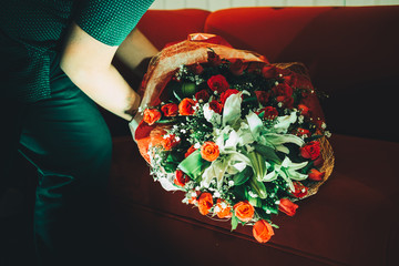 Body part of a young man places a bouquet of roses on the red sofa. Selected focus.
