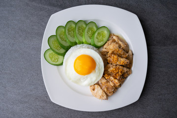 Rice,Fried egg,Fried chicken with garlic and black pepper in white dish on the concrete table.