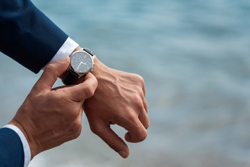 A man in a business suit checking a wrist watch on his hand on background  sea - obrazy, fototapety, plakaty