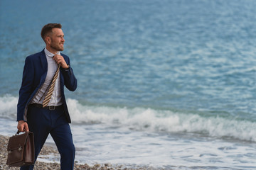 Businessman walking on the beach holding in hand briefcase