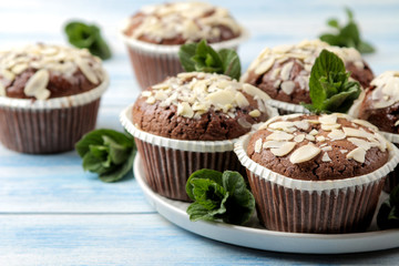 Delicious, sweet chocolate muffins, with almond petals and mint on a blue wooden table.