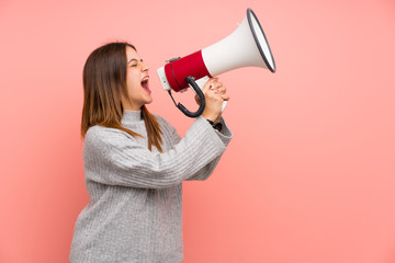 Young woman over pink wall shouting through a megaphone