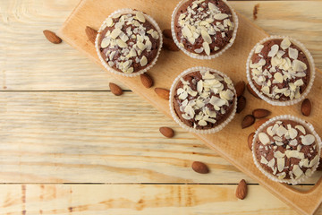 Delicious, sweet chocolate muffins, with almond petals next to almond nuts on a natural wooden table. top view