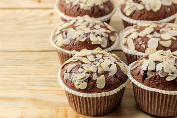 Delicious, sweet chocolate muffins, with almond petals next to almond nuts on a natural wooden table. close-up