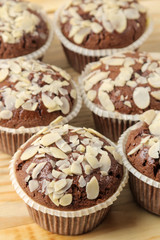 Delicious, sweet chocolate muffins, with almond petals next to almond nuts on a natural wooden table. close-up