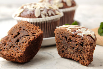 Delicious, sweet chocolate muffins, with almond petals next to mint and almond nuts on a light concrete table. close-up