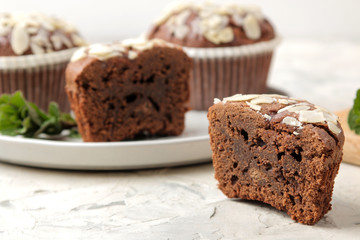Delicious, sweet chocolate muffins, with almond petals next to mint and almond nuts on a light concrete table. close-up