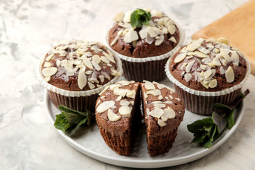 Delicious, sweet chocolate muffins, with almond petals next to mint and almond nuts on a light concrete table. close-up