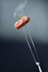 smoking hot slice of red marbled beef steak at meat fork decorated with rosemary. Minimal meat...