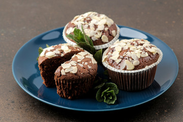 Delicious, sweet chocolate muffins, with almond petals next to mint and almond in a plate on a dark table.