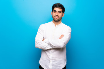 Young man over isolated blue wall keeping the arms crossed in frontal position