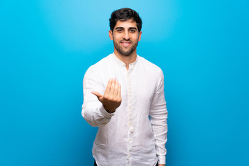 Young man over isolated blue wall inviting to come with hand. Happy that you came
