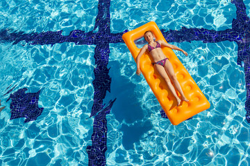The girl relaxes on an orange inflatable mattress in the pool, taking air baths.