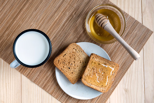 Two Slices of Toast Bread with Tin Mug of Milk and Jar of Honey on a Wooden Table Setup