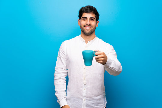 Young Man Over Isolated Blue Wall Holding A Hot Cup Of Coffee