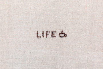 Life word with a cup made from coffee beans on linen texture, arranged in center.