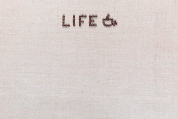Life word with a cup made from coffee beans on linen texture, arranged top center.
