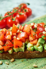 On a green plate of brusket with tomatoes and avocado. Light gray textured background. Beautiful serving of dishes. Restaurant menu