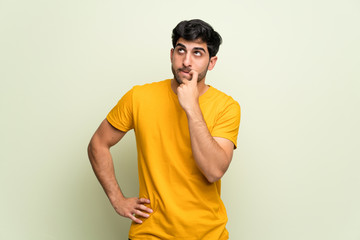 Young man over pink wall having doubts while looking up
