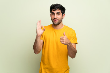 Young man over pink wall showing ok sign with and giving a thumb up gesture