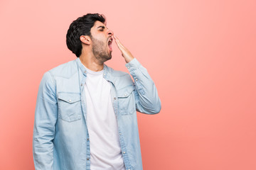 Young man over pink wall yawning and covering wide open mouth with hand