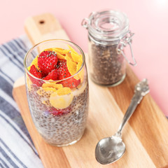 Chia pudding parfait with banana, strawberry, chia seeds and cornflakes on a wooden cutting board on pink background