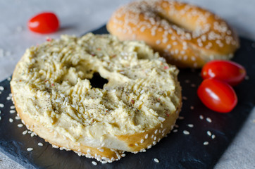 Bagel with hummus, spices and sesame seeds, cherry tomatoes on the black stone desk. Close up.