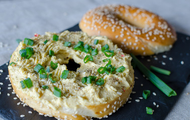 Bagel with hummus, spices, green onion  and sesame seeds on the black stone desk. Close up.