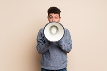 Young man over isolated wall shouting through a megaphone
