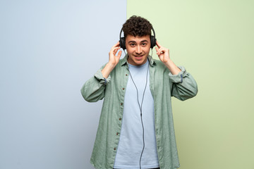 Young man over blue and green background listening to music with headphones