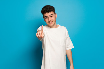 Young man over blue background showing and lifting a finger